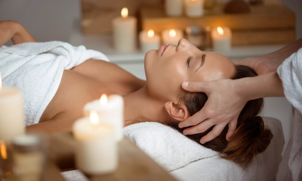 A woman receiving a relaxing head massage in a serene spa setting, surrounded by softly glowing candles.