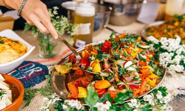 A vibrant platter of fresh, colorful salad with assorted vegetables, herbs, and flowers, accompanied by various condiments in the background.