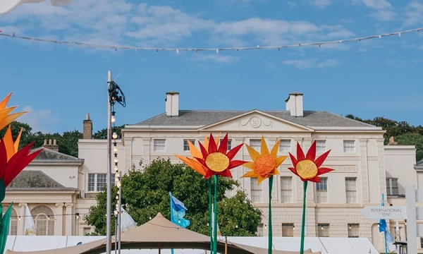 Colorful flower sculptures in front of a large, elegant white building with trees and a blue sky in the background.