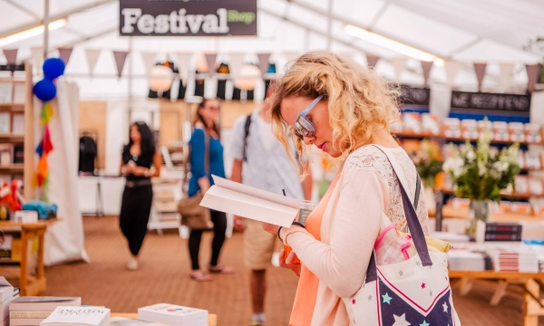 A woman with curly hair examines a book inside a brightly lit tented area, surrounded by book displays and festival decorations.