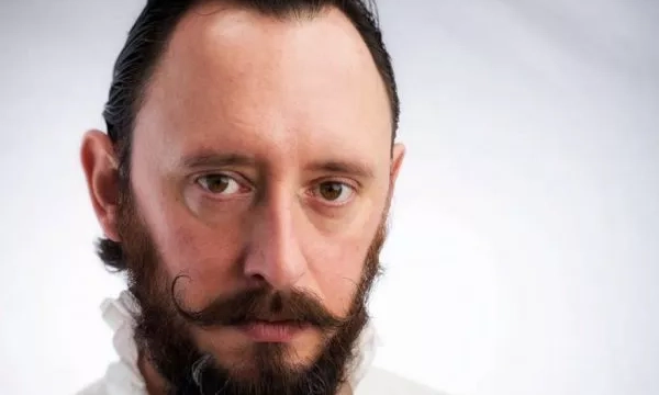 Portrait of a man with a well-groomed beard and mustache, wearing a white ruffled collar, against a neutral background.