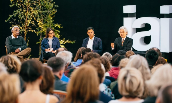A panel discussion featuring four speakers, including a middle-aged man with gray hair, a woman with glasses, a younger man, and an older man with white hair, in front of an audience.